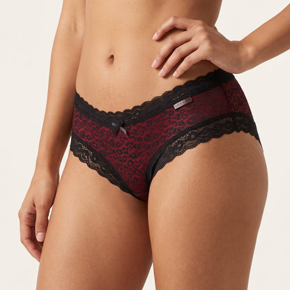 A model wearing red and black leopard print lace panties against a light beige studio background.