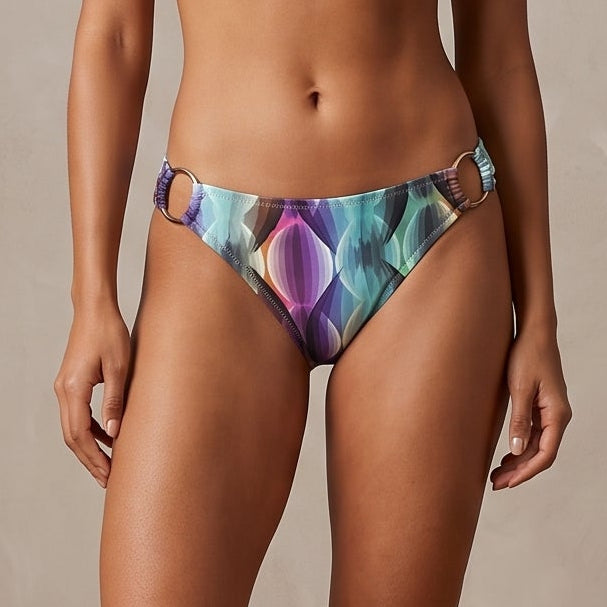 A woman stands barefoot in a studio wearing a two-piece bikini with a colorful abstract cosmic pattern in purple, blue, teal, and pink. Text in the lower right reads 'THE COSMIC WAVE SET'.