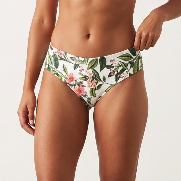 A woman modeling a two-piece bikini set in a studio setting. The top is a solid white scoop-neck bikini top, and the bottoms feature a tropical floral print with green leaves and pink flowers on a white background.